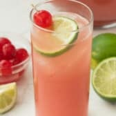 pink drink in a tall clear glass with a lime and a cherry inside.