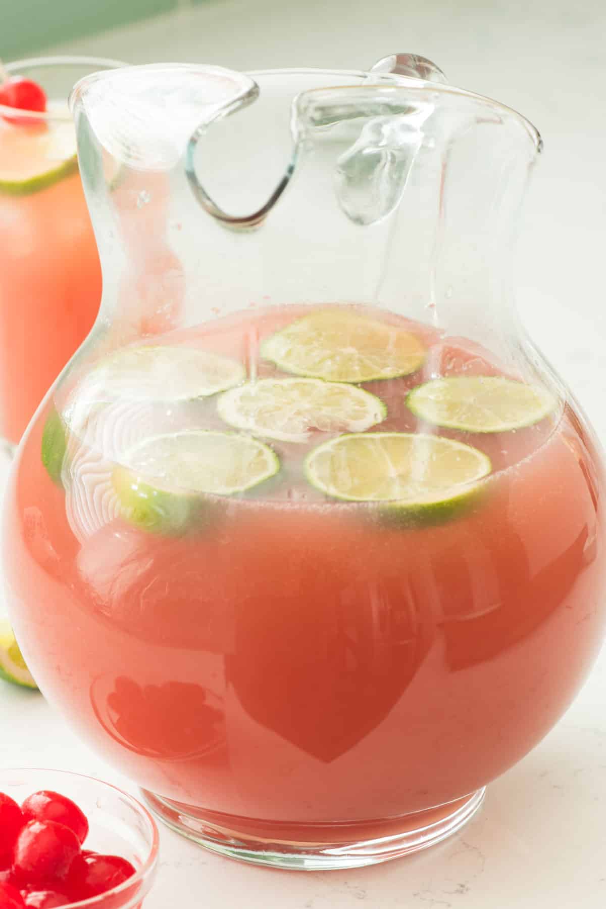 pink drink in a clear big pitcher with sliced limes inside.