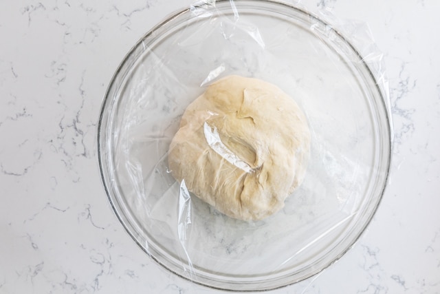 dough in bowl with plastic wrap.