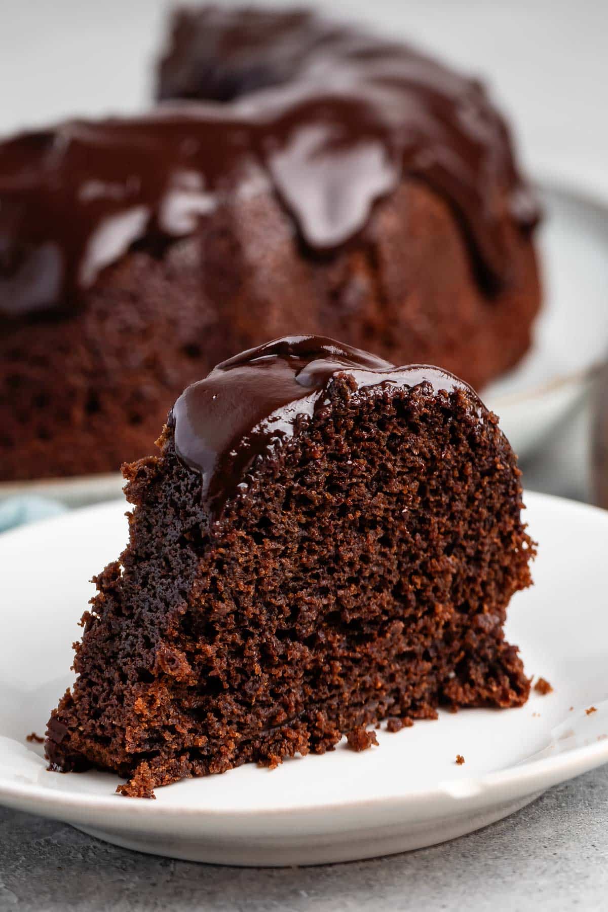 slice of chocolate cake on a white plate with a chocolate glaze on top.