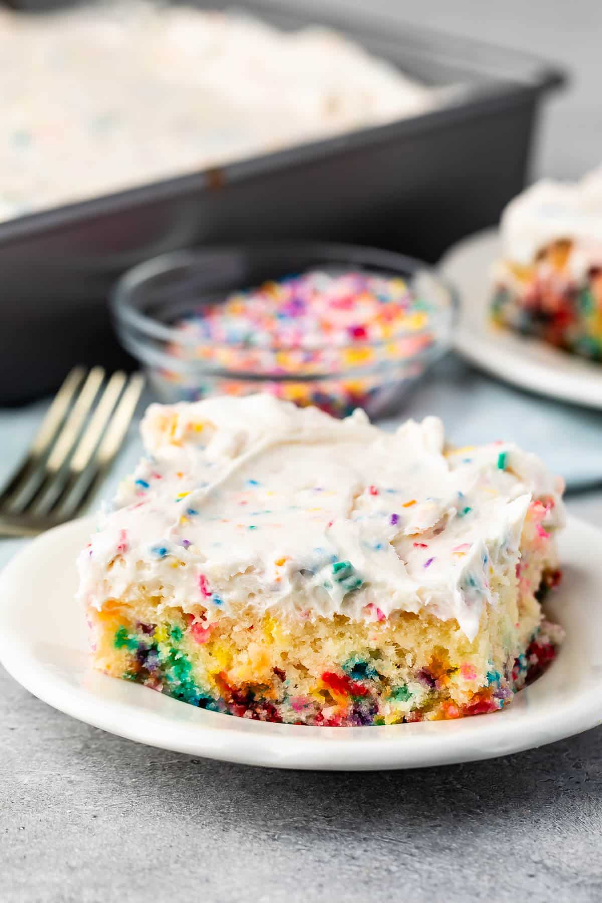 white cake with colorful sprinkles baked in and white frosting with more sprinkles mixed in on top.