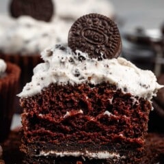 chocolate cupcake split in half with white Oreo frosting and a mini Oreo on top.