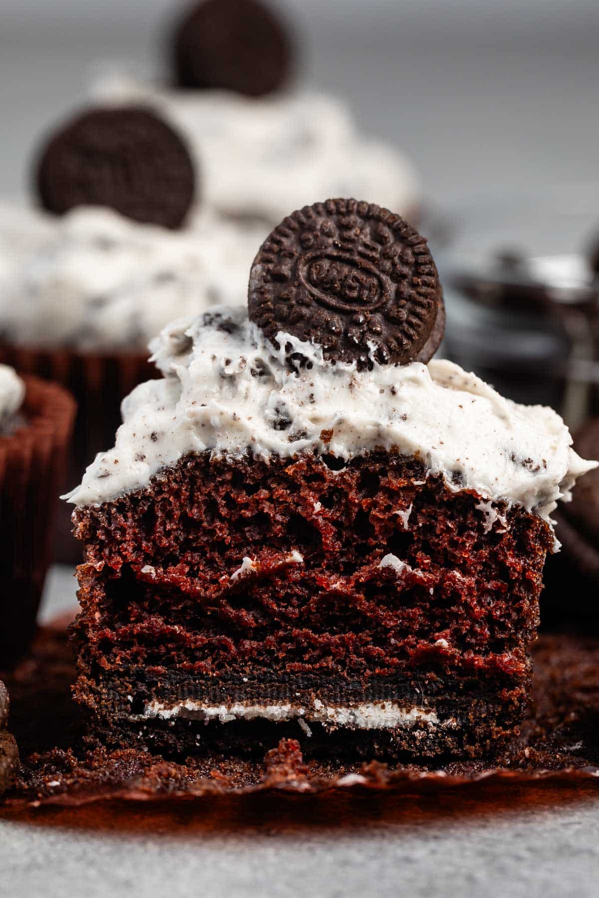chocolate cupcake split in half with white Oreo frosting and a mini Oreo on top.
