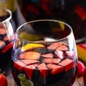 dark red wine in a short clear glass with fruit chopped up inside.