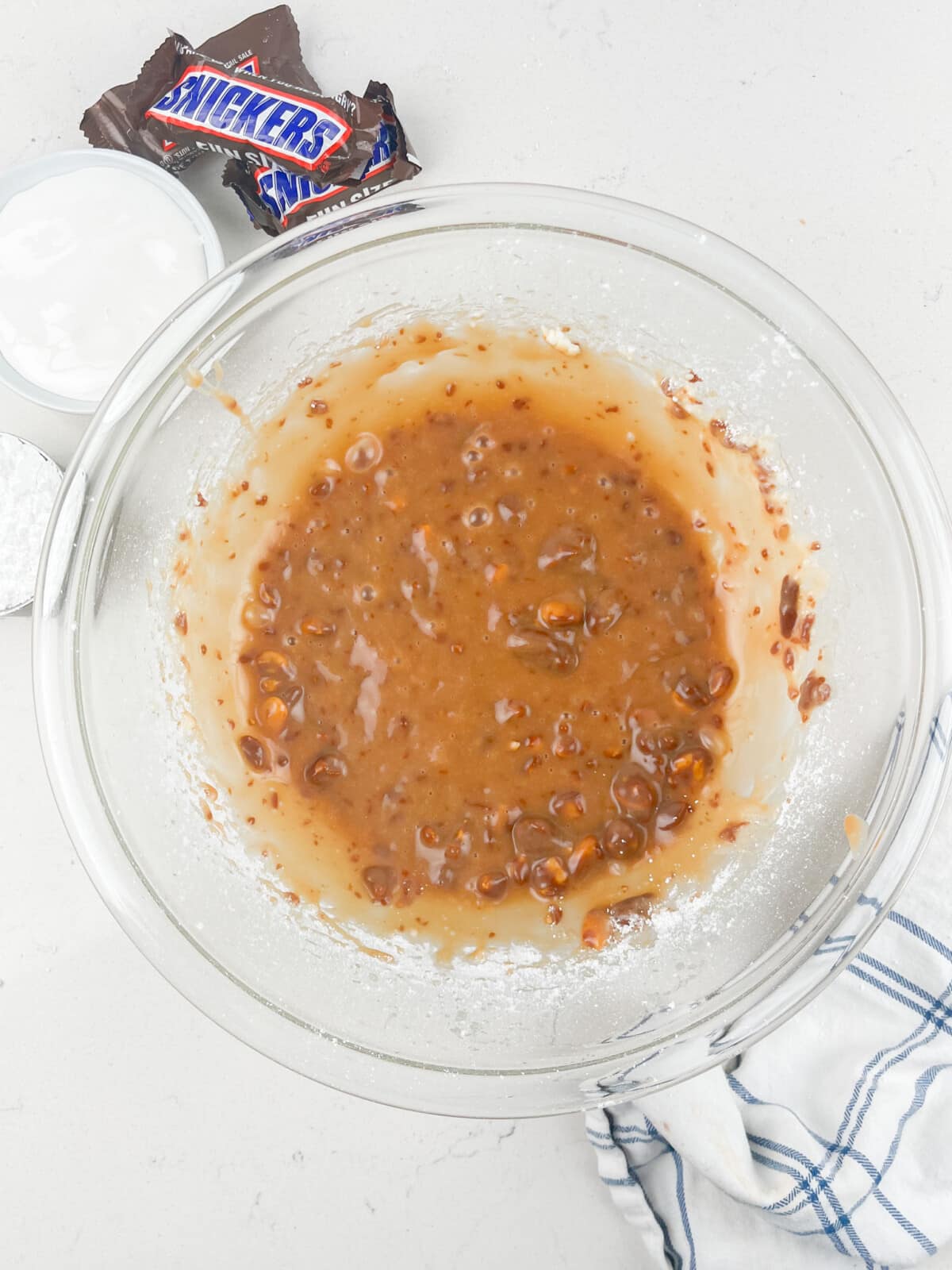 process shot of snickers dip being made on a white marble counter.