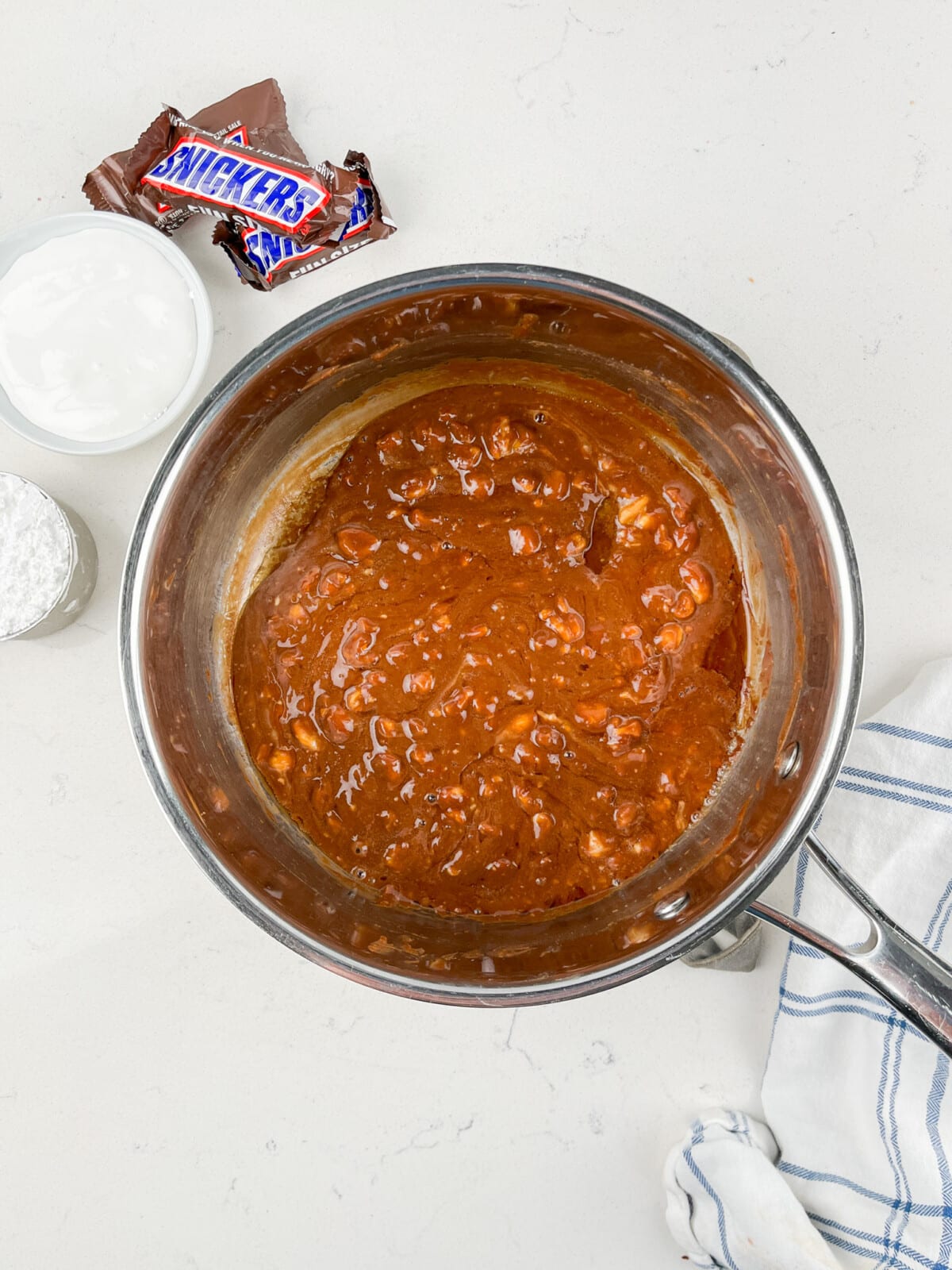 process shot of snickers dip being made on a white marble counter.