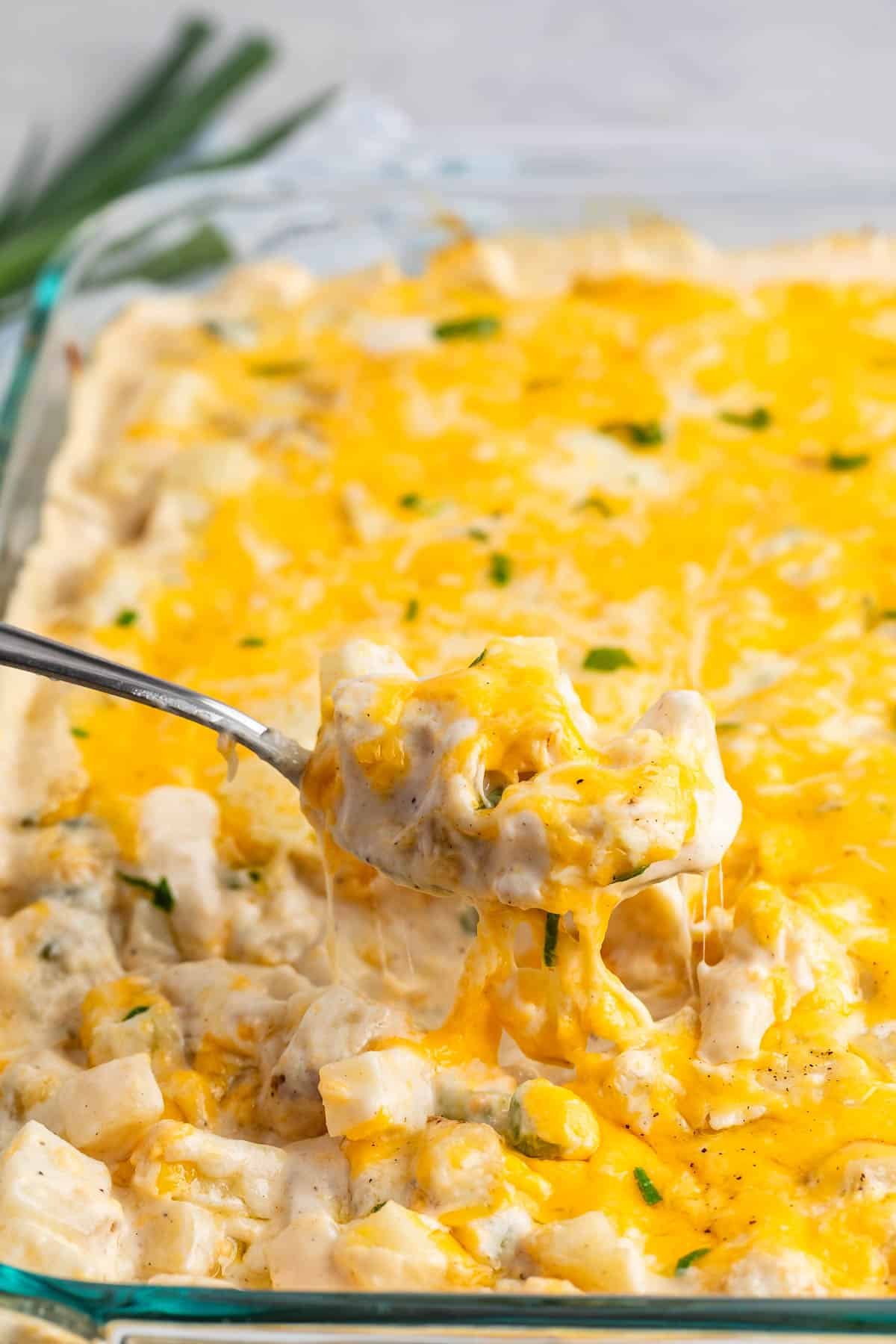 cheesy potato casserole in a clear casserole pan with green garnish.