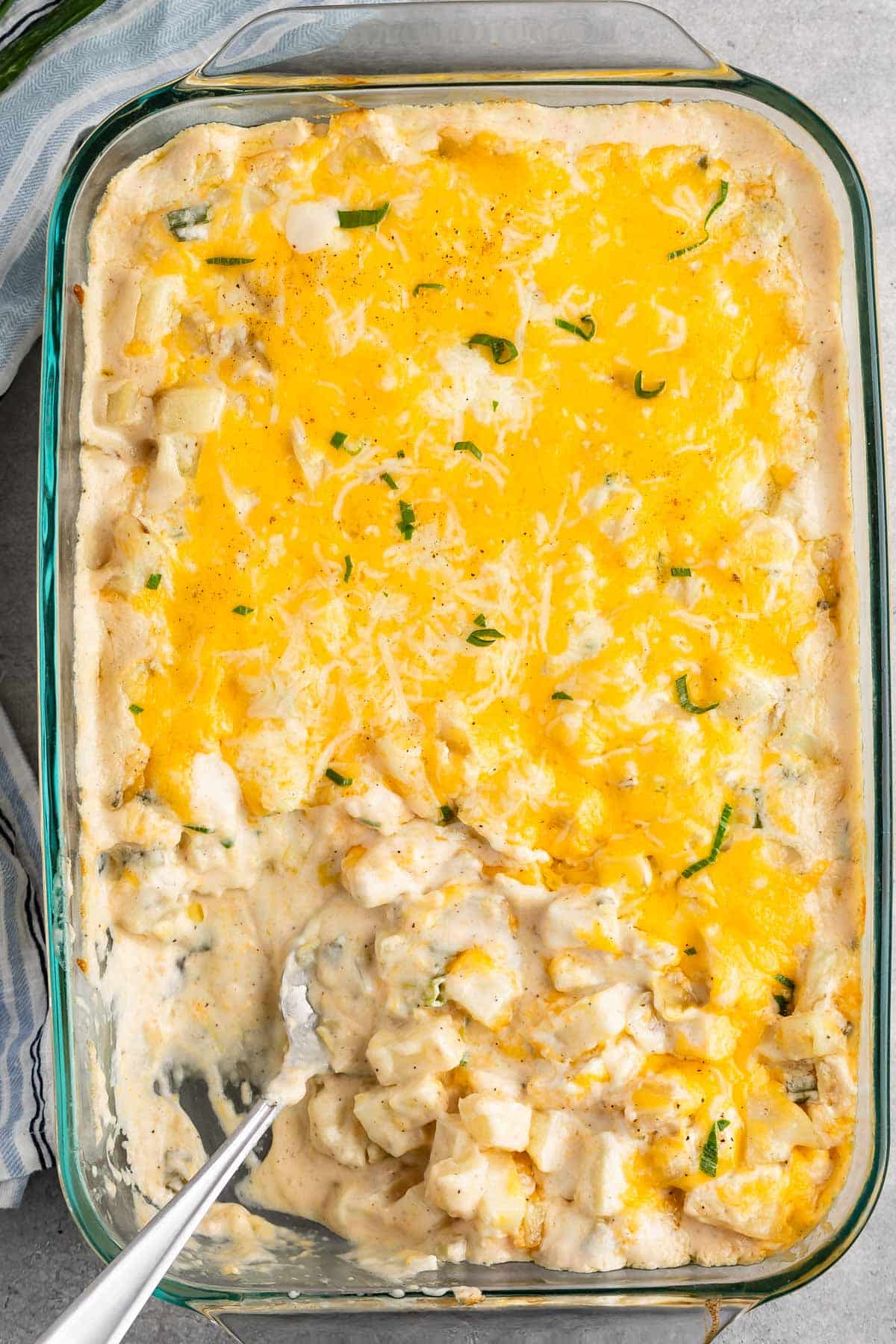 cheesy potato casserole in a clear casserole pan with green garnish.