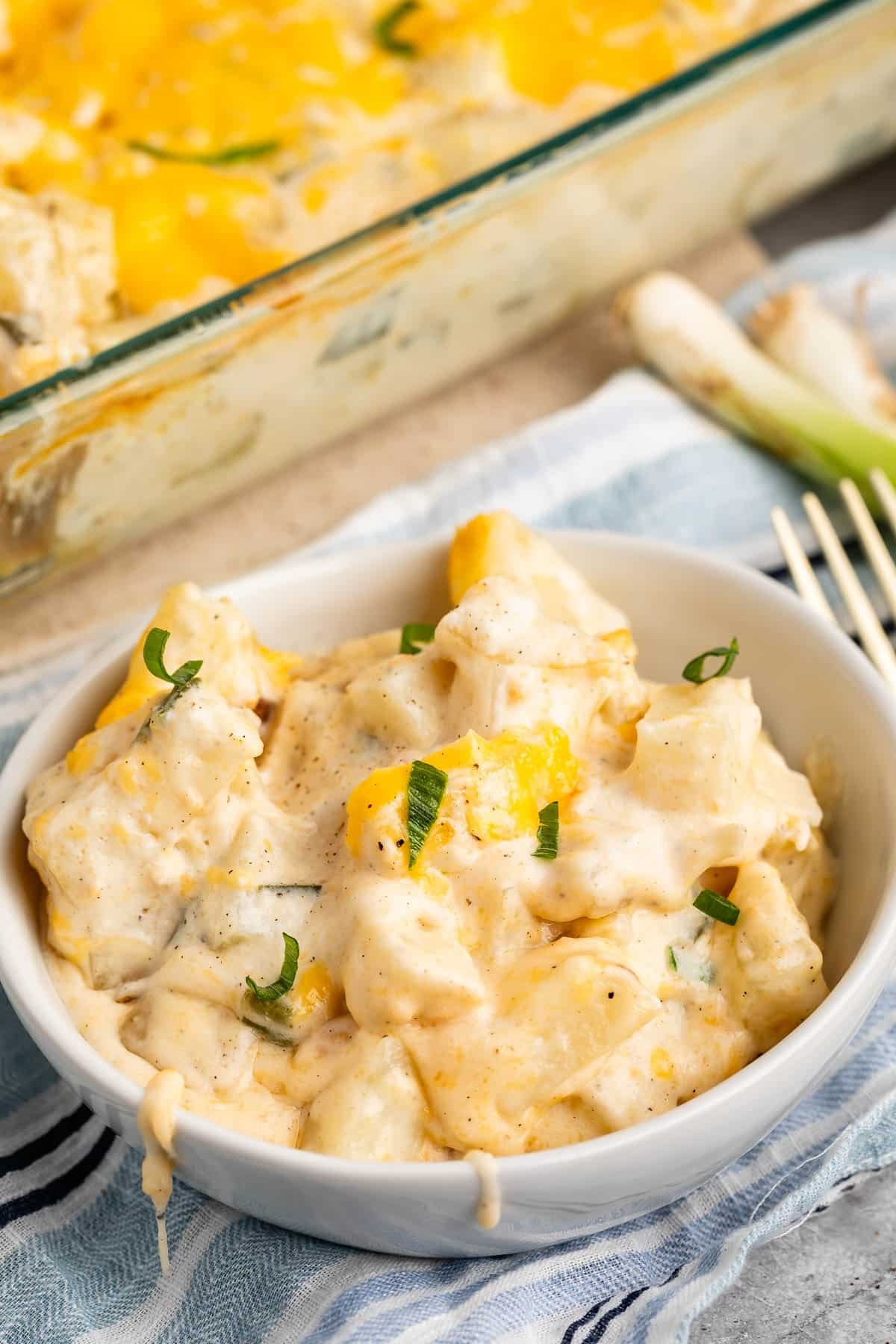 cheesy potatoes in a white bowl with green garnish.
