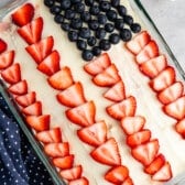 cake with white frosting and sliced strawberry and blueberries on top to make an American flag.