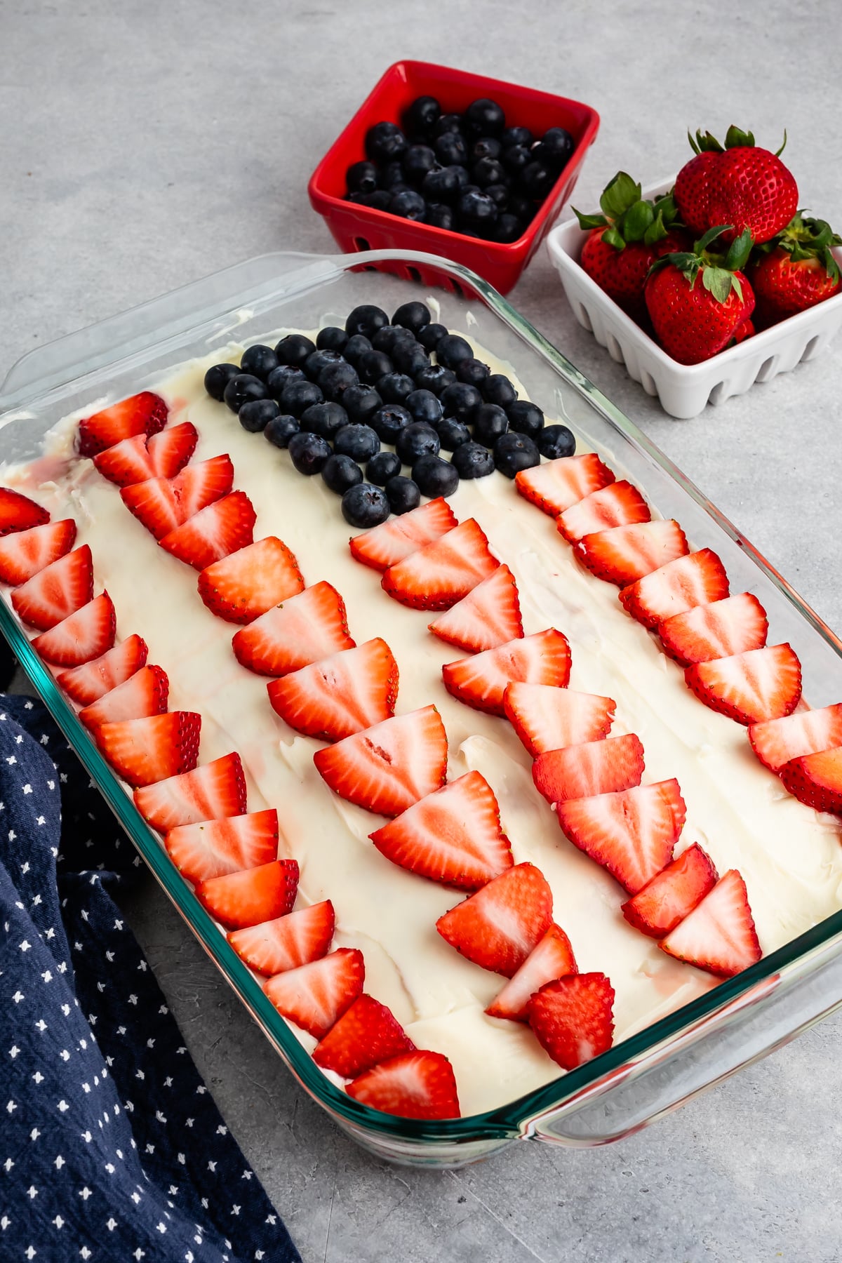 cake with white frosting and sliced strawberry and blueberries on top to make an American flag.