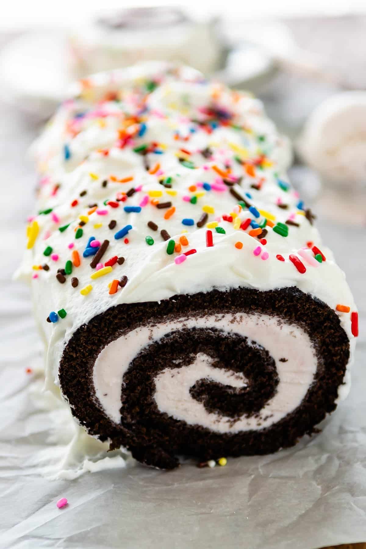 chocolate cake roll covered in white frosting and colorful sprinkles.