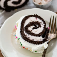 chocolate cake roll covered in white frosting and colorful sprinkles.