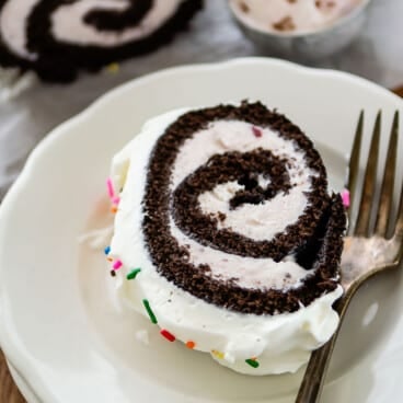 chocolate cake roll covered in white frosting and colorful sprinkles.