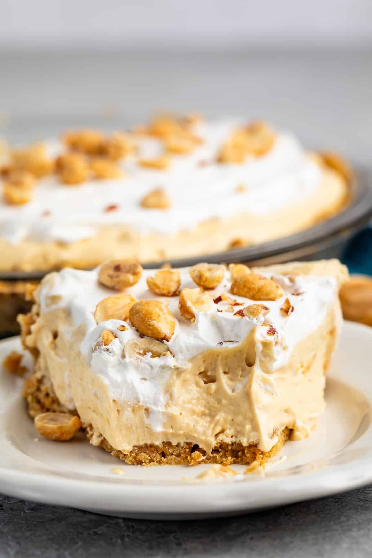peanut butter pie on a white plate with peanuts on top.
