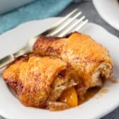 two crescent roll dumplings on a white plate next to a fork.
