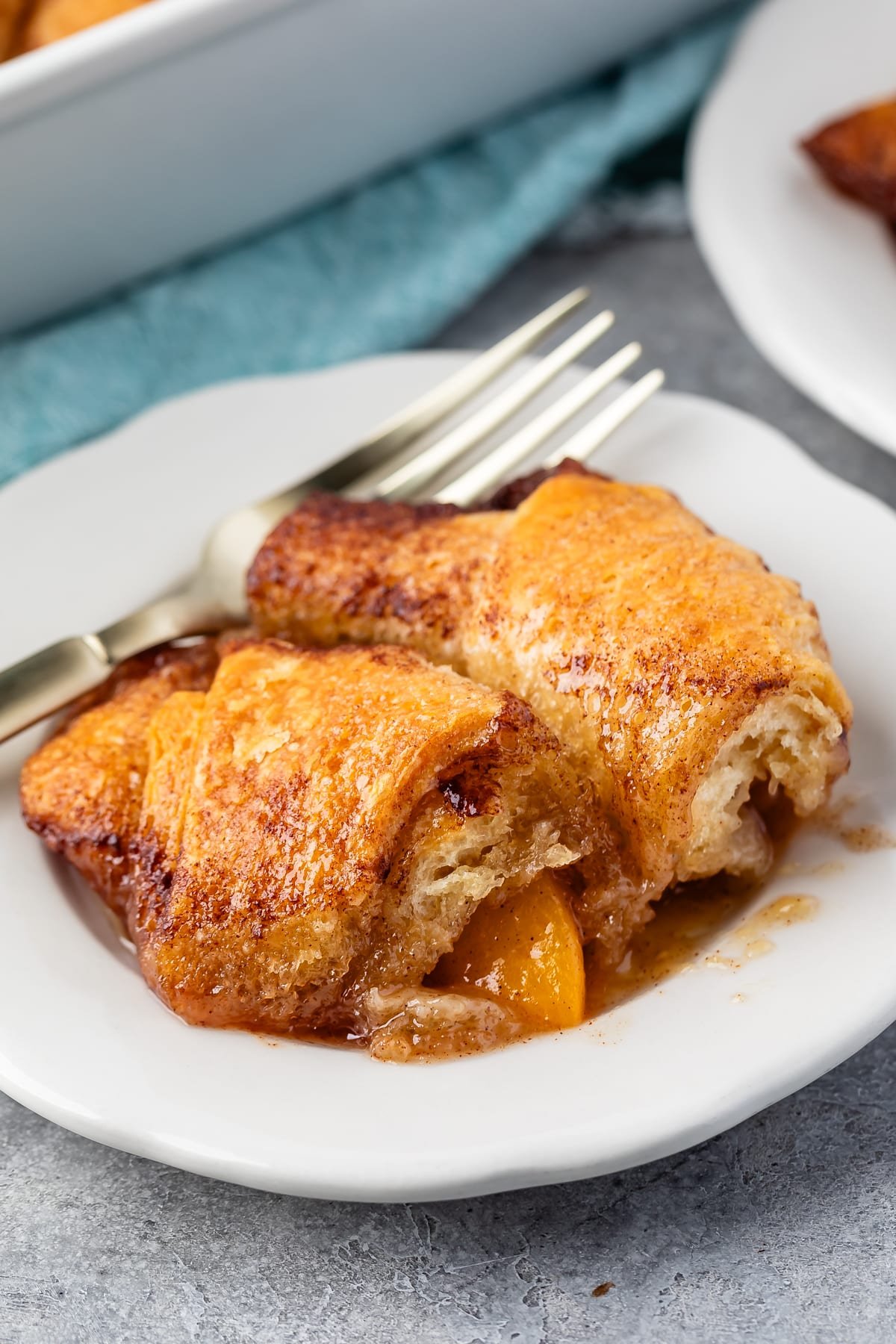 two crescent roll dumplings on a white plate next to a fork.