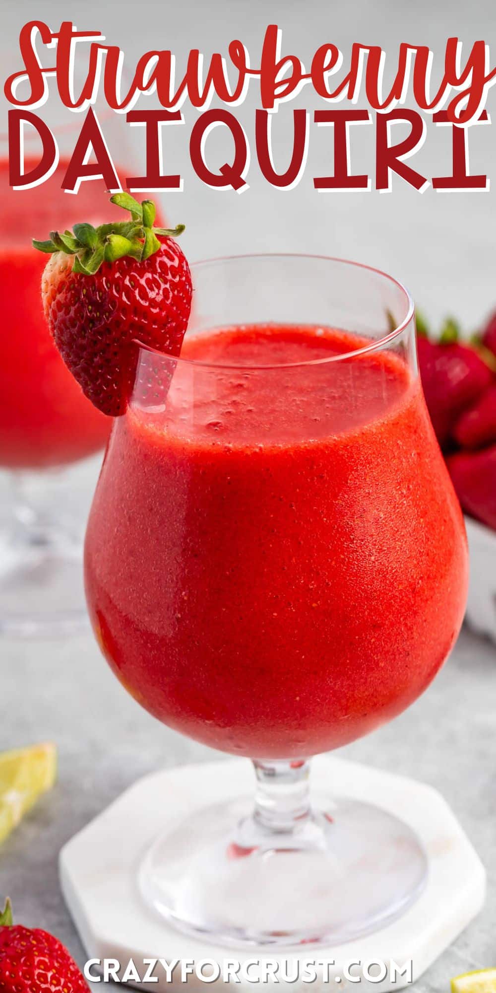 strawberry daiquiri in a stout clear glass with lemon and strawberries around and on the rim with words on the image.