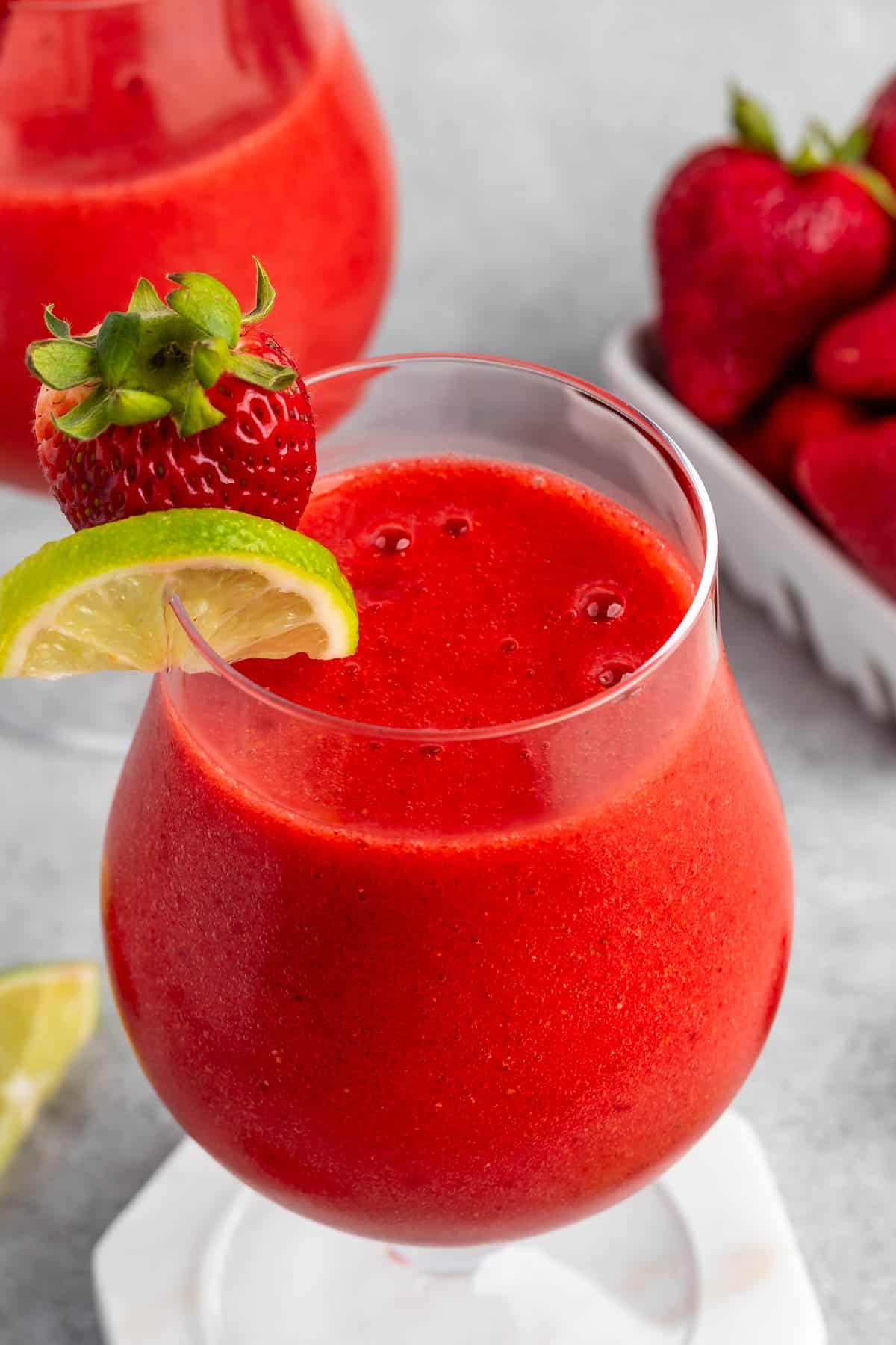 strawberry daiquiri in a stout clear glass with lemon and strawberries around and on the rim.