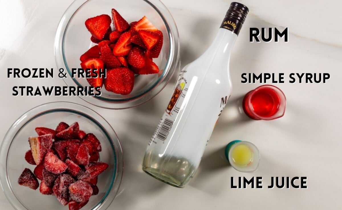 ingredients in strawberry daiquiri laid out on a white marble counter.