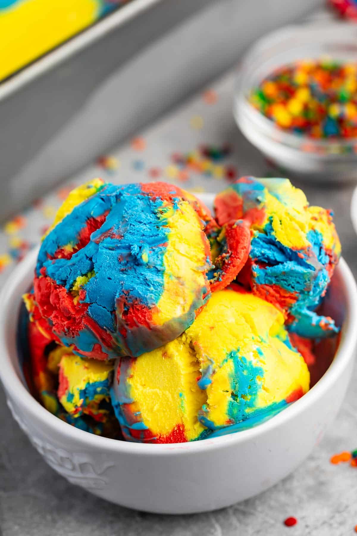 many scoops of red and yellow and blue ice cream mixed in a white bowl.