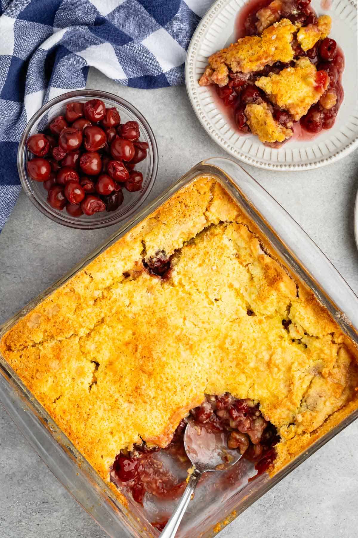 overhead shot of a tart cherry cobbler in a clear 9x13 pan with a silver spoon.