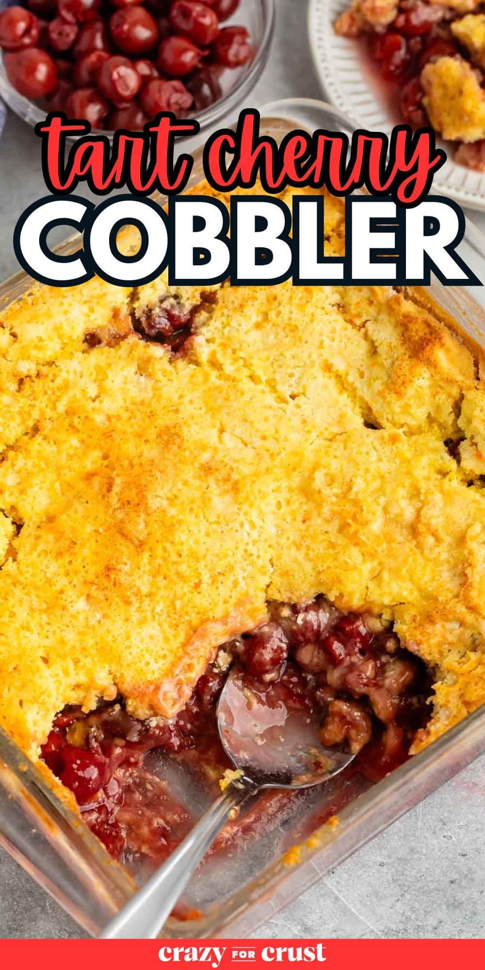 overhead shot of a tart cherry cobbler in a clear 9x13 pan with a silver spoon with words on the image.