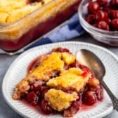 tart cherry cobbler on a grey plate next to a silver spoon.