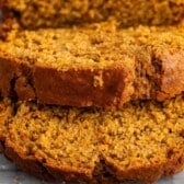 Close-up of several slices of moist, golden brown pumpkin banana bread resting on a sheet of parchment paper. The texture looks soft and slightly crumbly.