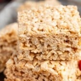Close-up of two stacked pumpkin Rice Krispie treats, showcasing their marshmallow texture, with a small orange candy pumpkin in the background.