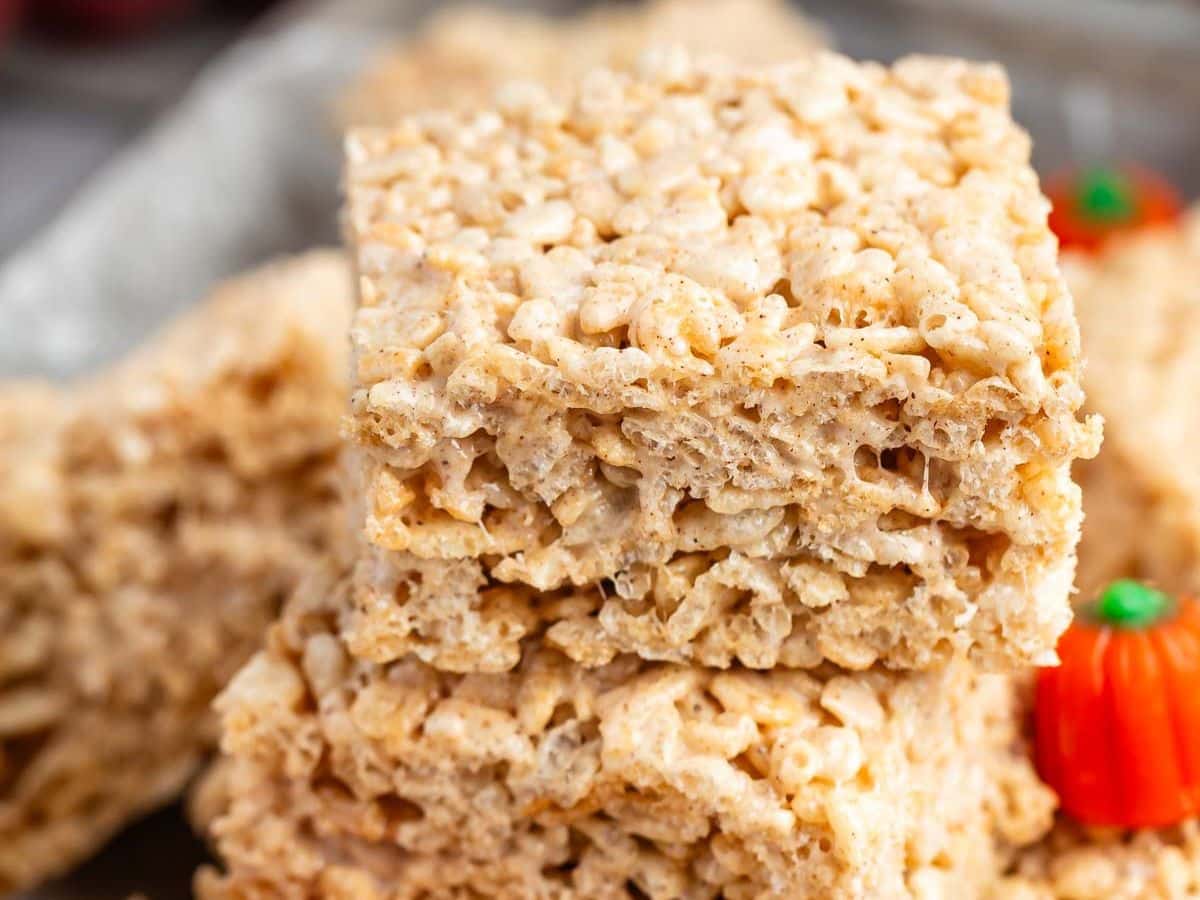 Close-up of two stacked pumpkin Rice Krispie treats, showcasing their marshmallow texture, with a small orange candy pumpkin in the background.