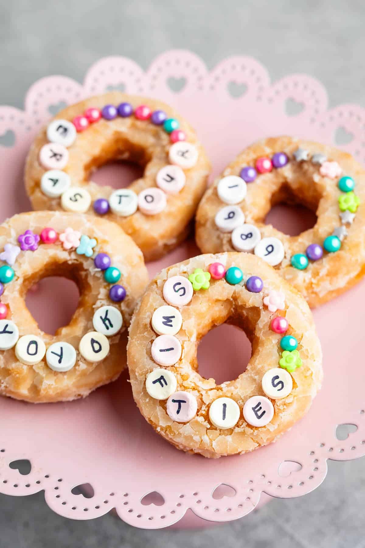 4 doughnuts on pink cake plate with sprinkles and candy.