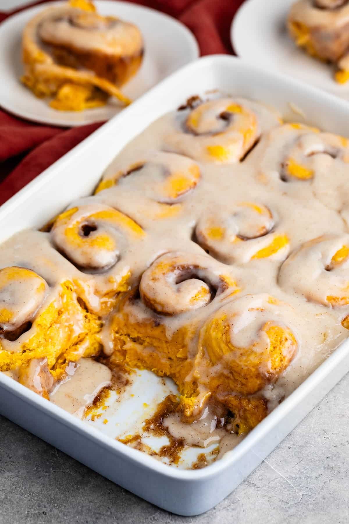 pumpkin cinnamon roll covered in glaze and cinnamon on a white pan.