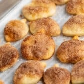 Bite-sized, acorn-shaped pie crust cookies sprinkled with cinnamon sugar are arranged on a parchment-lined baking tray.