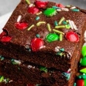 Two Christmas brownies stacked on a plate, topped with red and green candy-coated chocolate pieces and sprinkles.