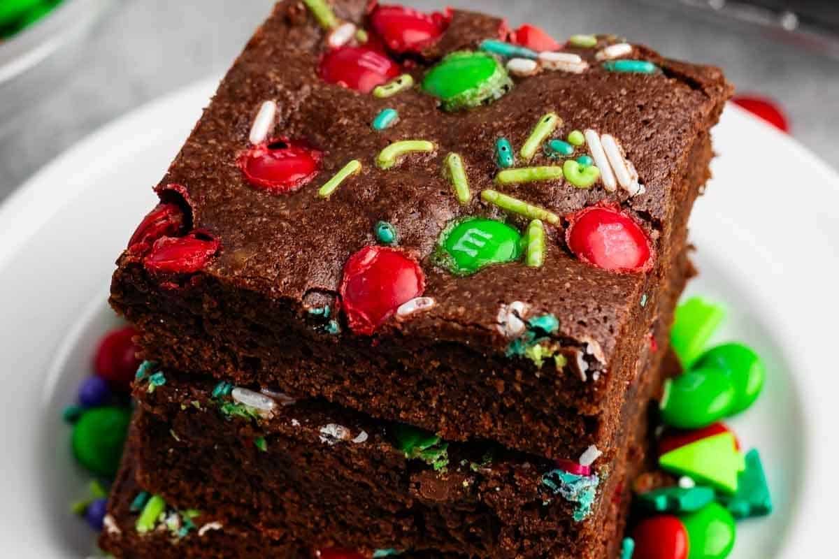 Two Christmas brownies stacked on a plate, topped with red and green candy-coated chocolate pieces and sprinkles.
