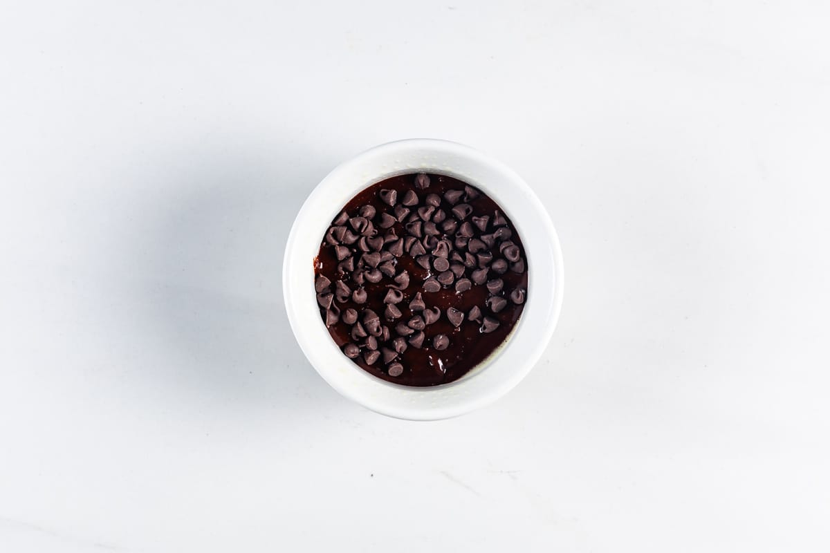 A white bowl filled with rich chocolate pudding, topped with a generous layer of chocolate chips, set against a plain white background.
