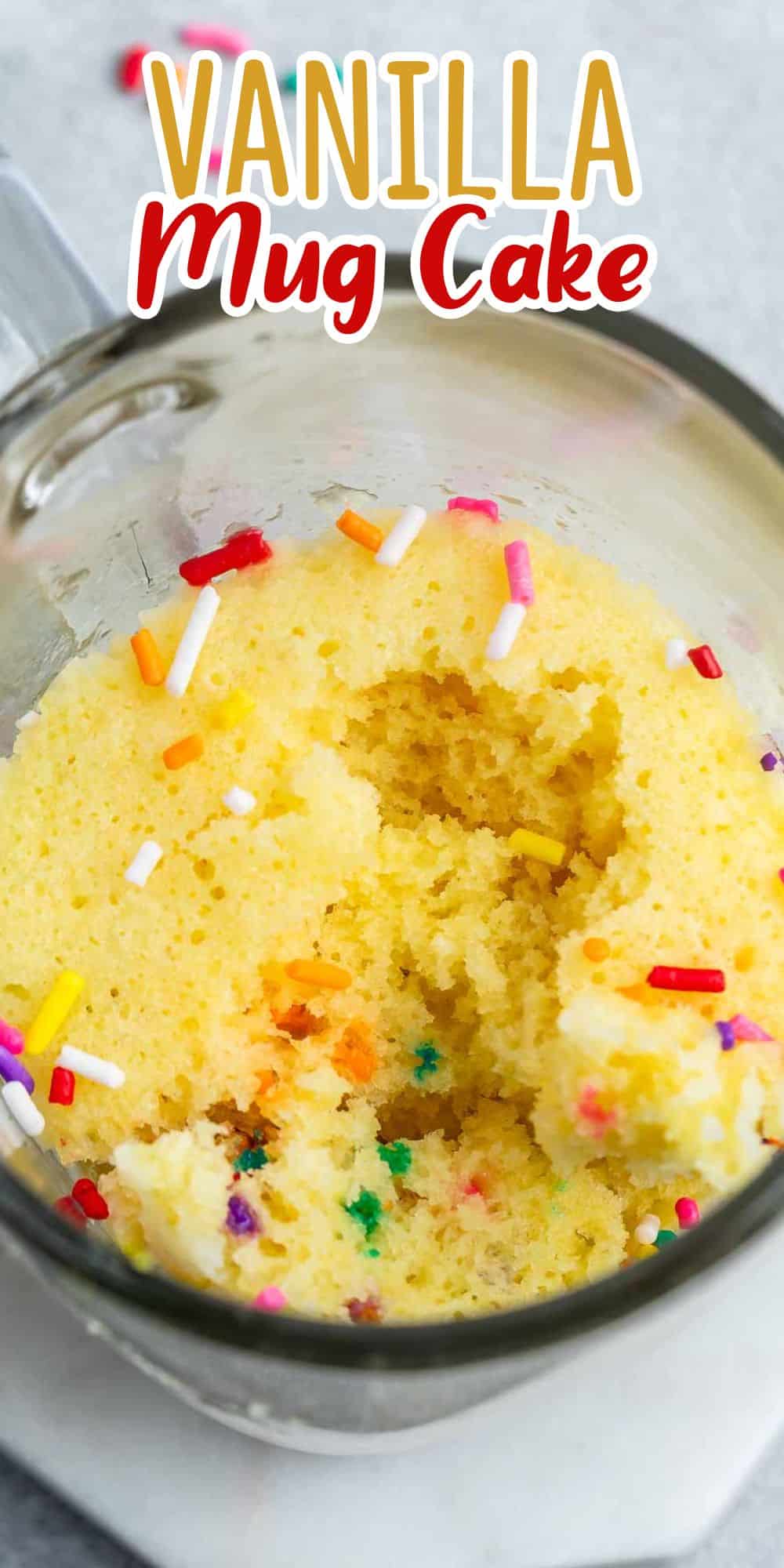 Mug filled with fluffy vanilla cake topped with colorful sprinkles. A bite is taken out, showing the cakes texture. Text overlay reads Vanilla Mug Cake.