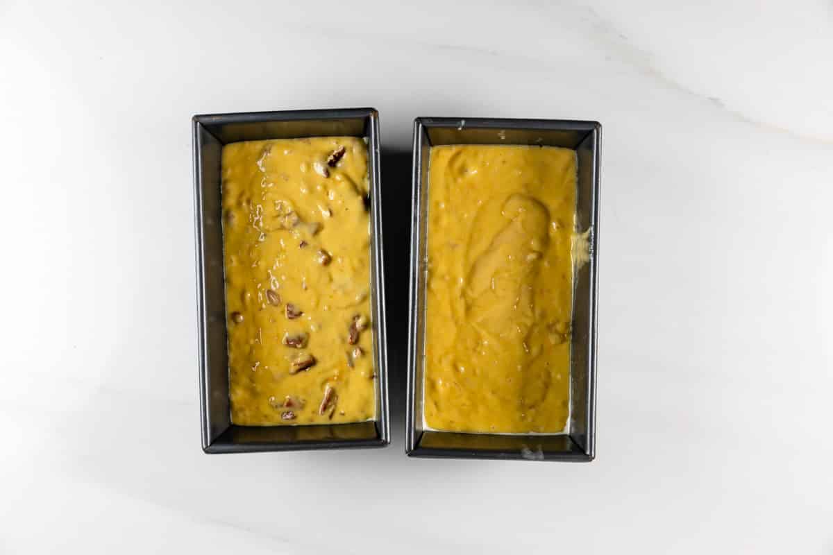 Two rectangular baking pans filled with unbaked batter sit on a white marble surface. The batter on the left contains visible nuts, while the batter on the right appears smooth.