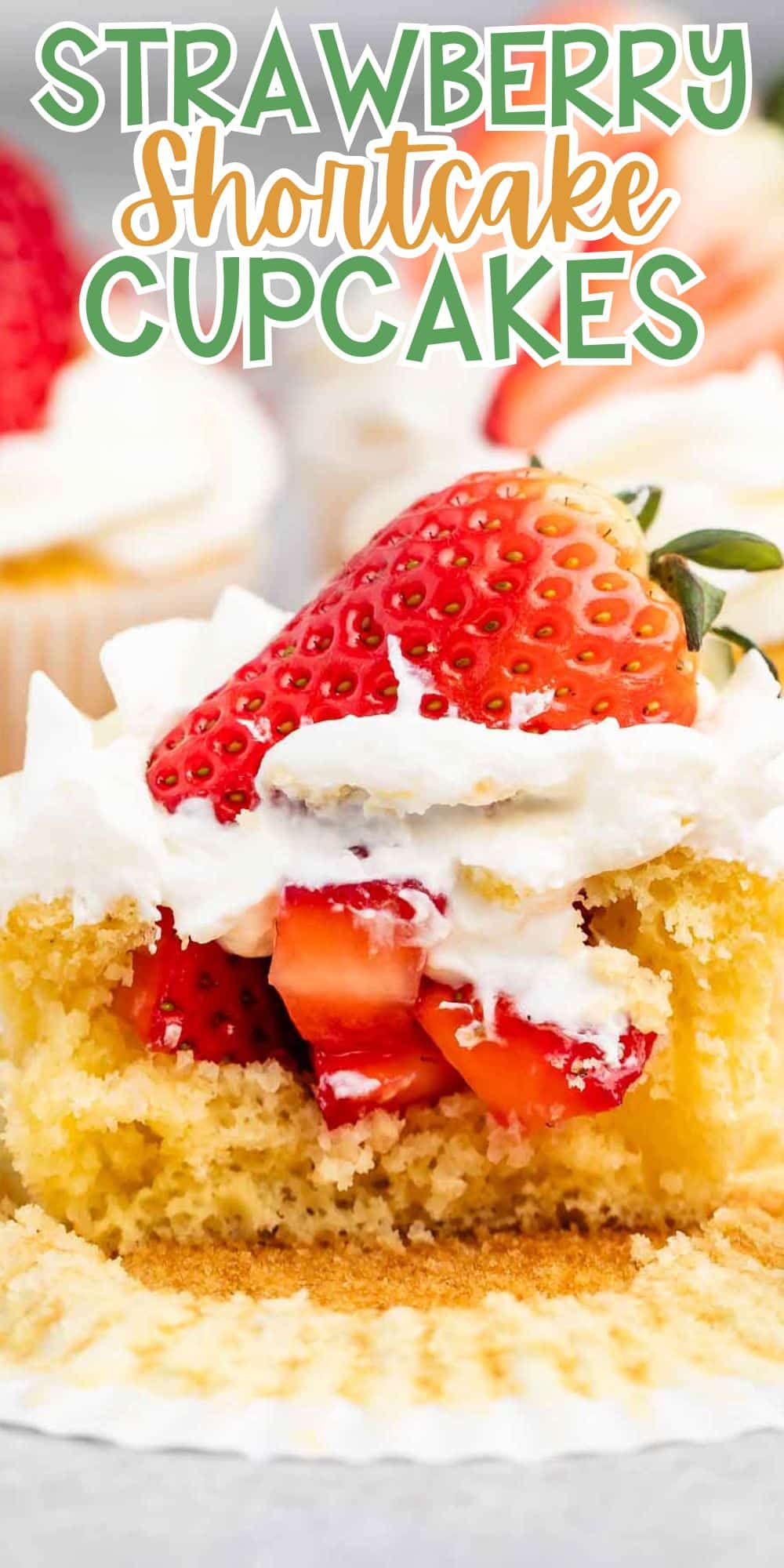 A close-up of a strawberry shortcake cupcake with whipped cream and sliced strawberries on top. The cupcake is partially unwrapped, revealing a fluffy cake and creamy filling. Text above reads, Strawberry Shortcake Cupcakes.