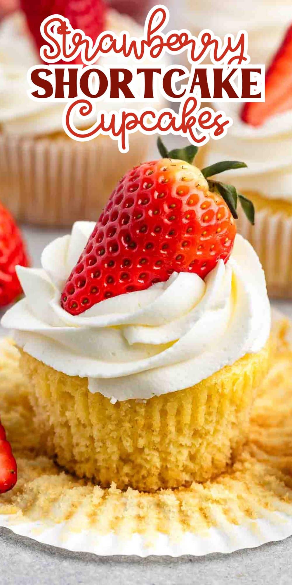 Vanilla cupcake with white frosting topped with a fresh strawberry, surrounded by more cupcakes. Text above reads Strawberry Shortcake Cupcakes.