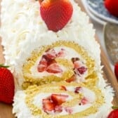 cake roll filled with strawberries and covered with white frosting on a cutting board.