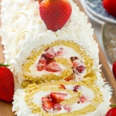 cake roll filled with strawberries and covered with white frosting on a cutting board.