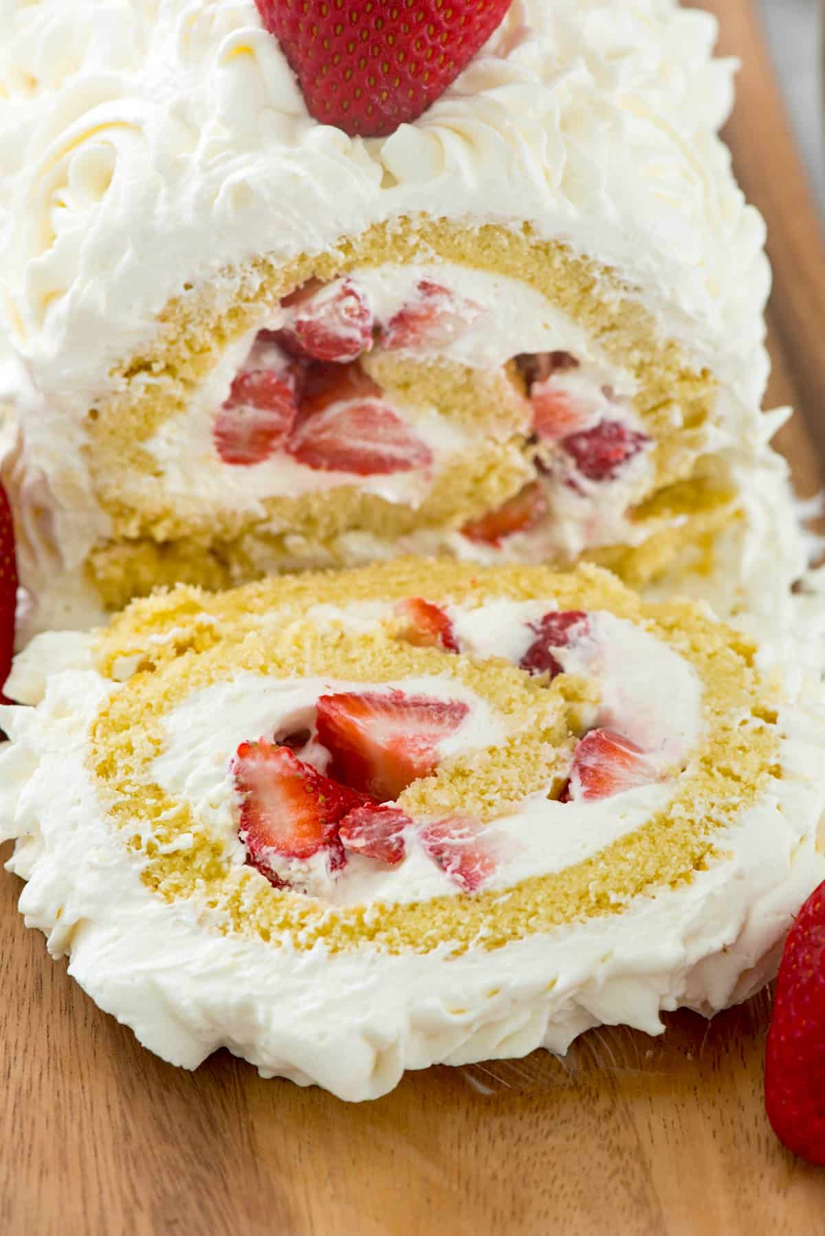 cake roll filled with strawberries and covered with white frosting on a cutting board.