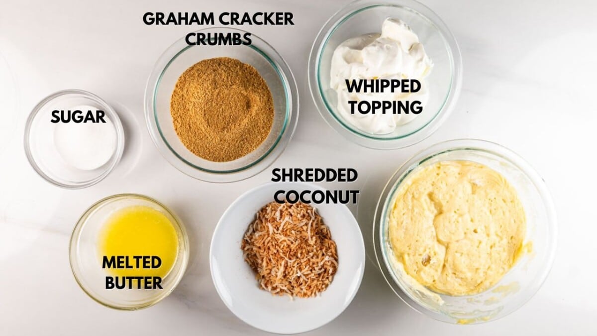 A top view of six bowls containing ingredients for a dessert on a white surface. They include graham cracker crumbs, whipped topping, sugar, melted butter, shredded coconut, and a yellow mixture. Each is labeled in bold, dark letters.