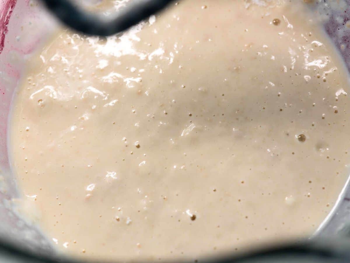 Close-up of a creamy, bubbly batter in a glass bowl, with visible air bubbles on the surface. The texture appears smooth and slightly thick, suggesting it’s a mixture ready for baking or cooking.