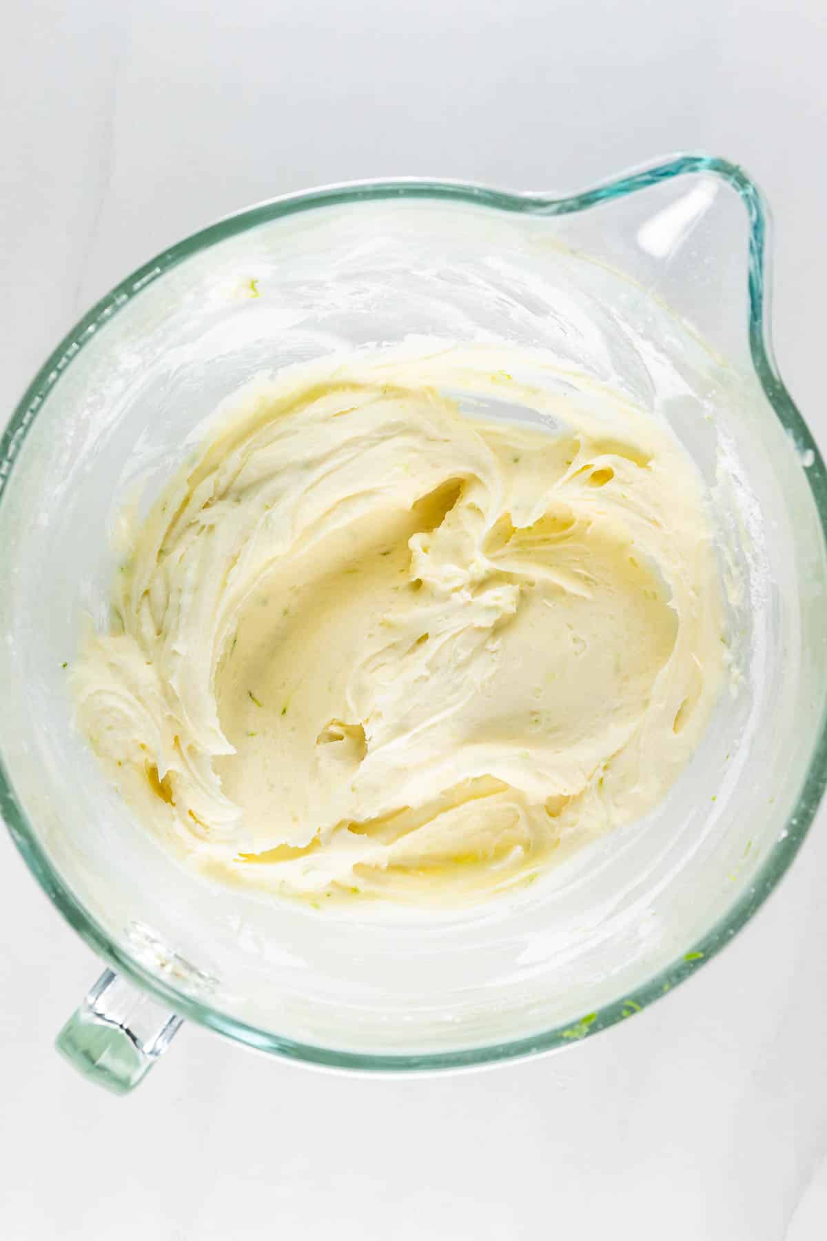 A glass bowl containing smooth, creamy cake batter with a pale yellow color. The texture is thick and swirled, suggesting it has been freshly mixed. The bowl sits on a white surface.