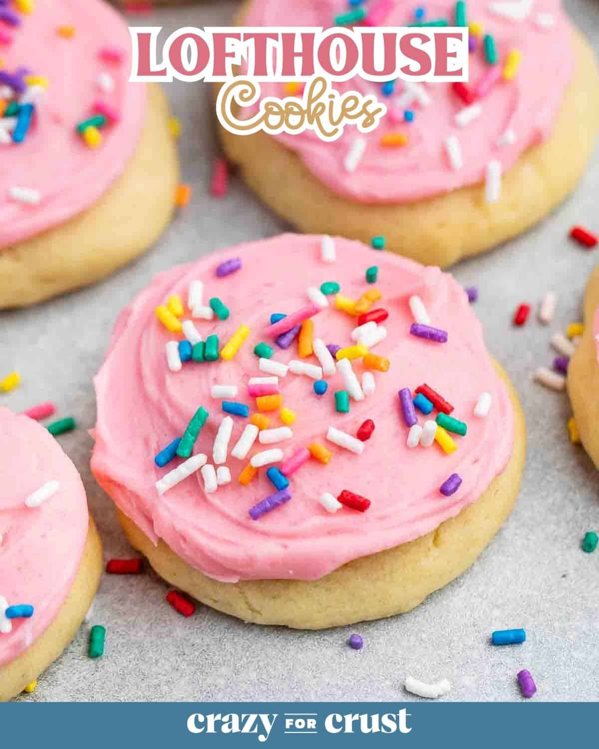 Close-up of soft sugar cookies with pink frosting and colorful sprinkles. The top of the image features the text Lofthouse Cookies, while the bottom reads crazy for crust. The cookies are on a lightly speckled surface.