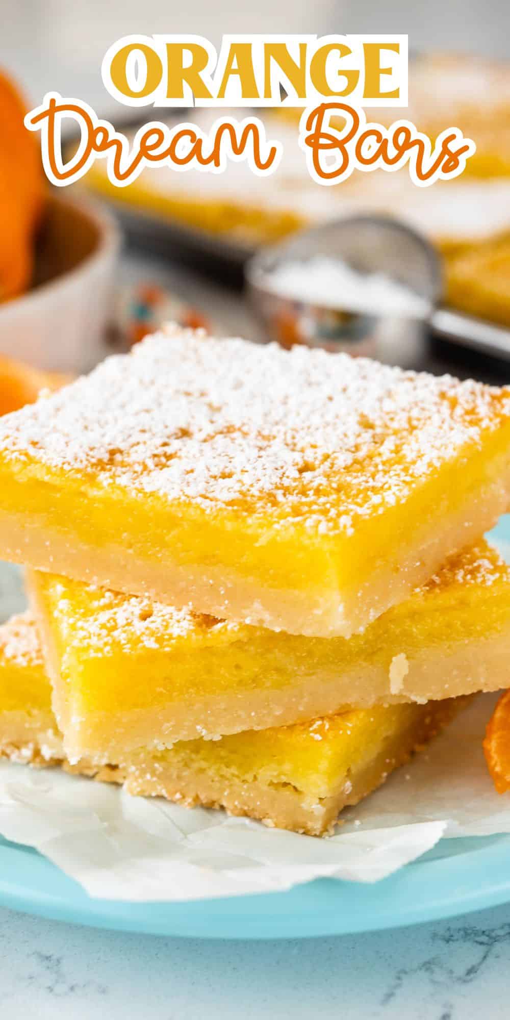 Three lemon bars stacked on a light blue plate, dusted with powdered sugar. In the background, there are sliced oranges, striped straws, and a small bowl of sugar on a white surface with words on the image.