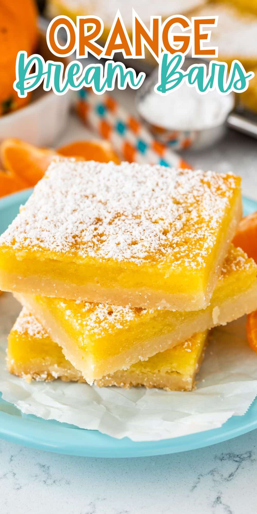 Three lemon bars stacked on a light blue plate, dusted with powdered sugar. In the background, there are sliced oranges, striped straws, and a small bowl of sugar on a white surface with words on the image.